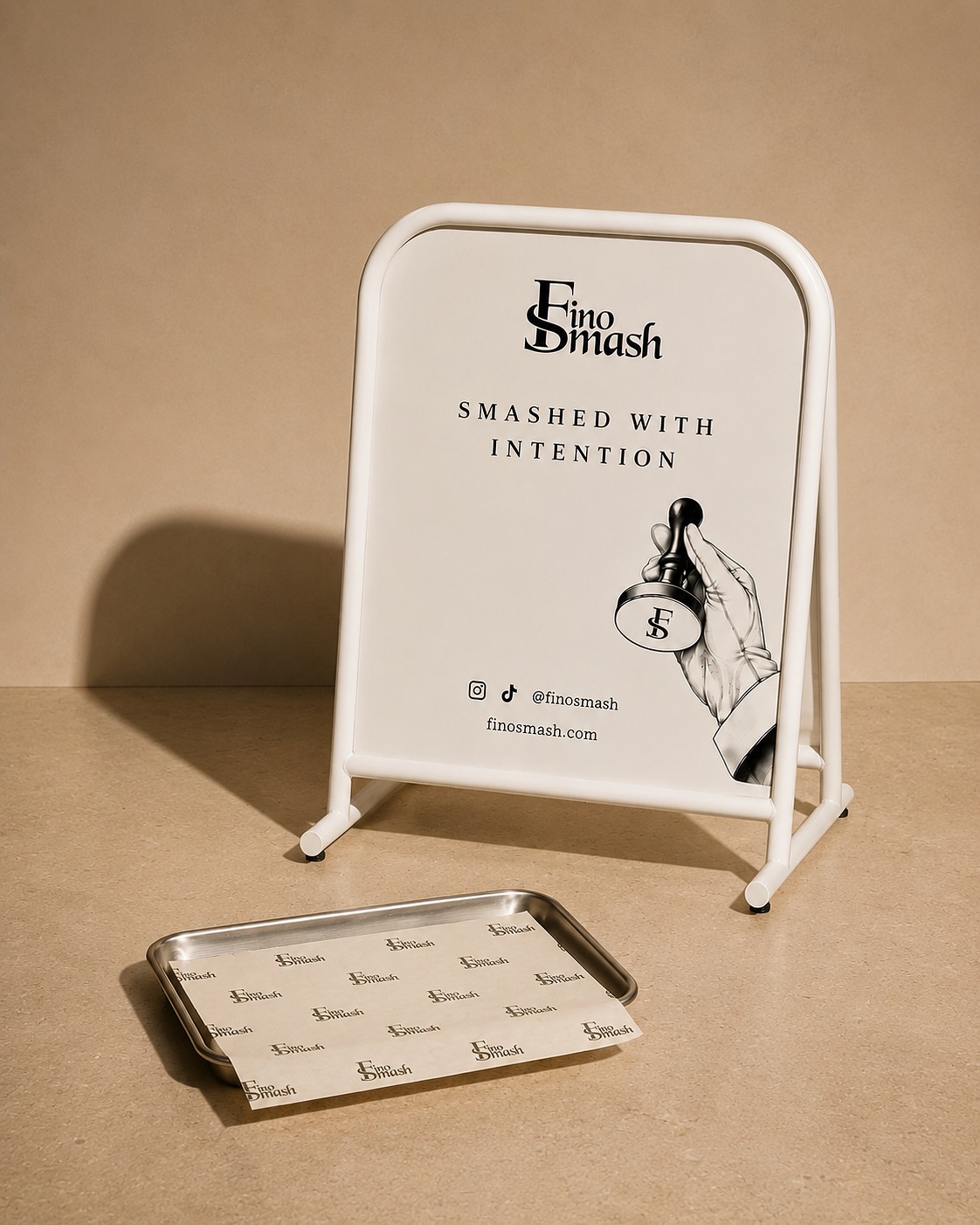 FinoSmash campaign: a cream FinoSmash A-board and a steel tray lined with printed FinoSmash paper against a warm beige wall